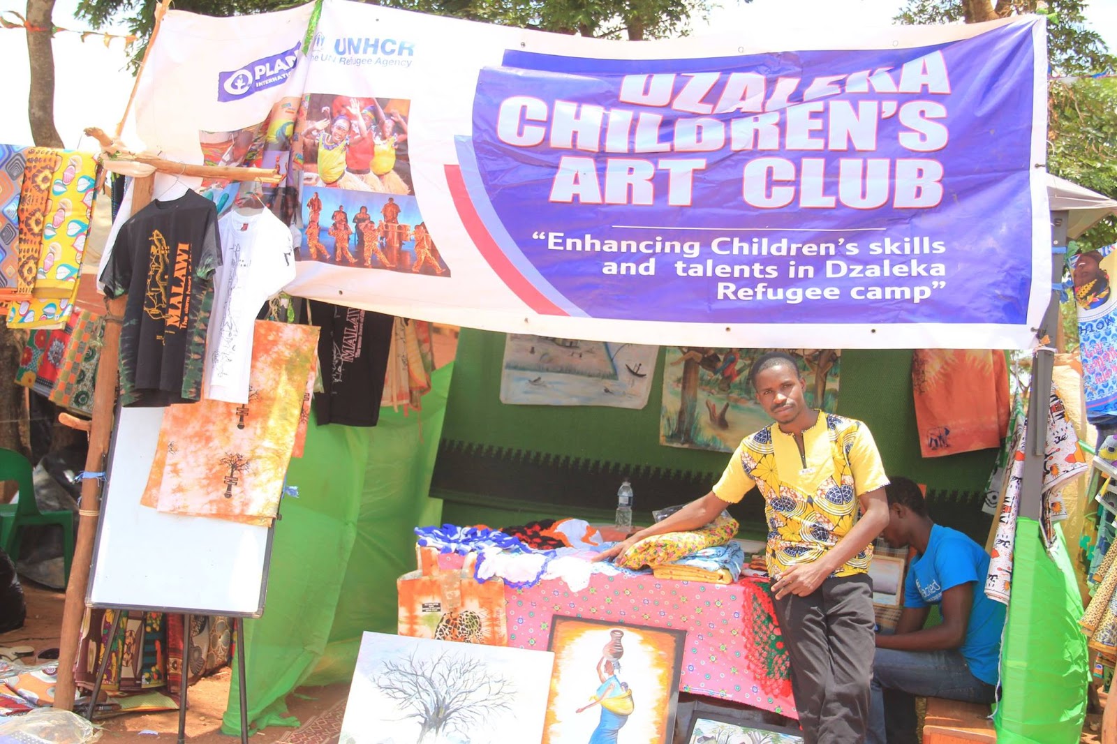 The Dzaleka Children's Art Club stall shows how performance, craft, and small-scale trade sit side by side.