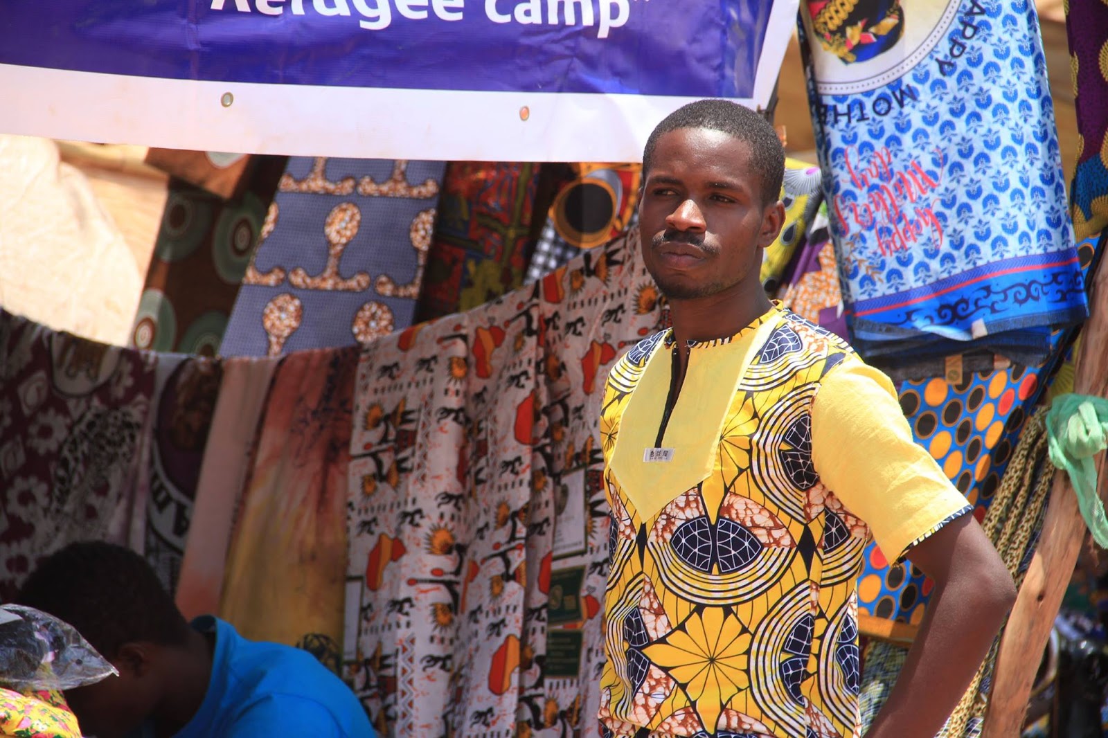 One vendor stands amid printed cloth and artwork, a reminder that the festival is also a working market.